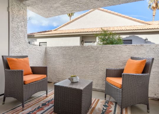 a patio with two chairs and a table with a potted plant on it
